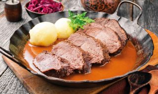 Traditional braised marinated German Sauerbraten from beef with potato dumplings and blue kraut in spicy brown sauce as closeup in a rustic wrought iron pan